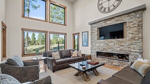 A spacious living room with a stone fireplace, large windows, and a comfortable seating area. - Luxury Sunriver Escape with Access to Exclusive Golf (Sunriver)