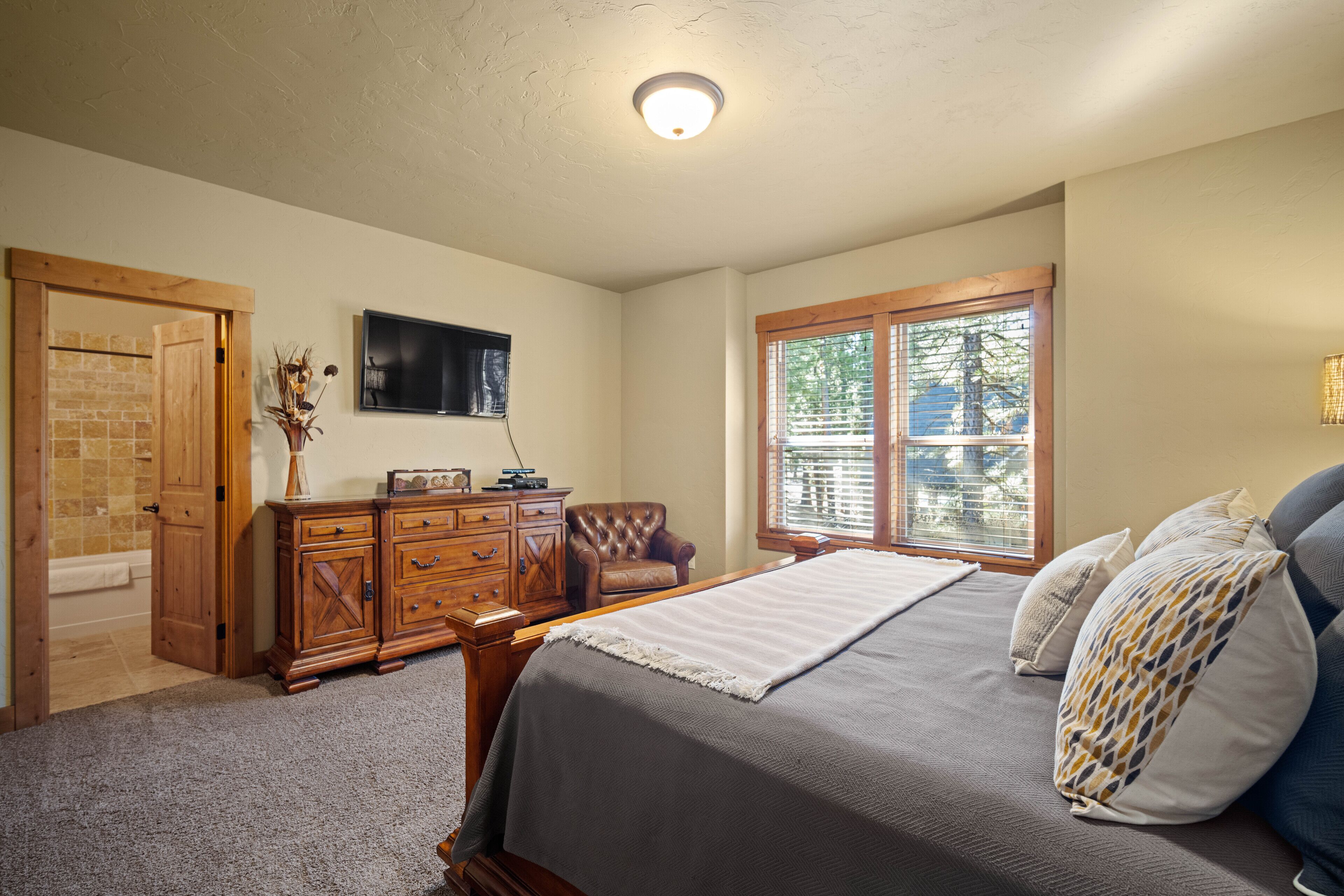 A bedroom with a bed, wooden dresser, and a television on the wall.