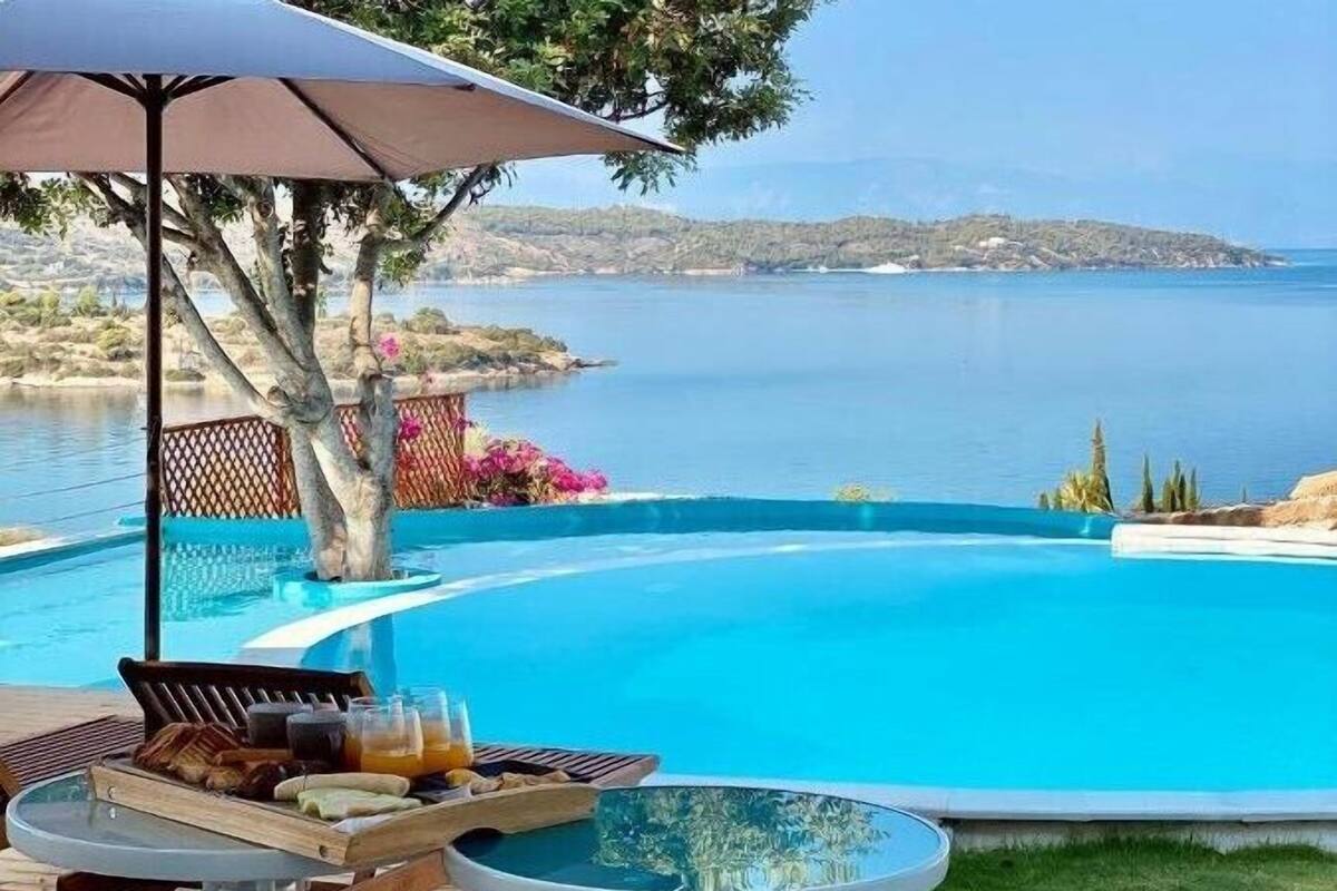 A poolside area with a table set for breakfast, a lounge chair, and a view of the sea.