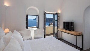 Une chambre d’hôtel comprenant un lit, un téléviseur posé sur une console en bois, un coin salon avec un fauteuil et un balcon offrant une vue sur la mer.