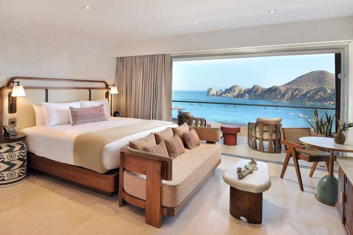 A hotel room with a large bed, a sofa, a dining area, and a view of the sea.
