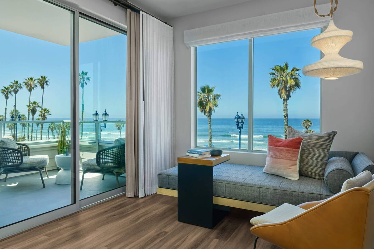 A modern room with a large window overlooking the beach, a sofa with cushions, and a small table with a book.