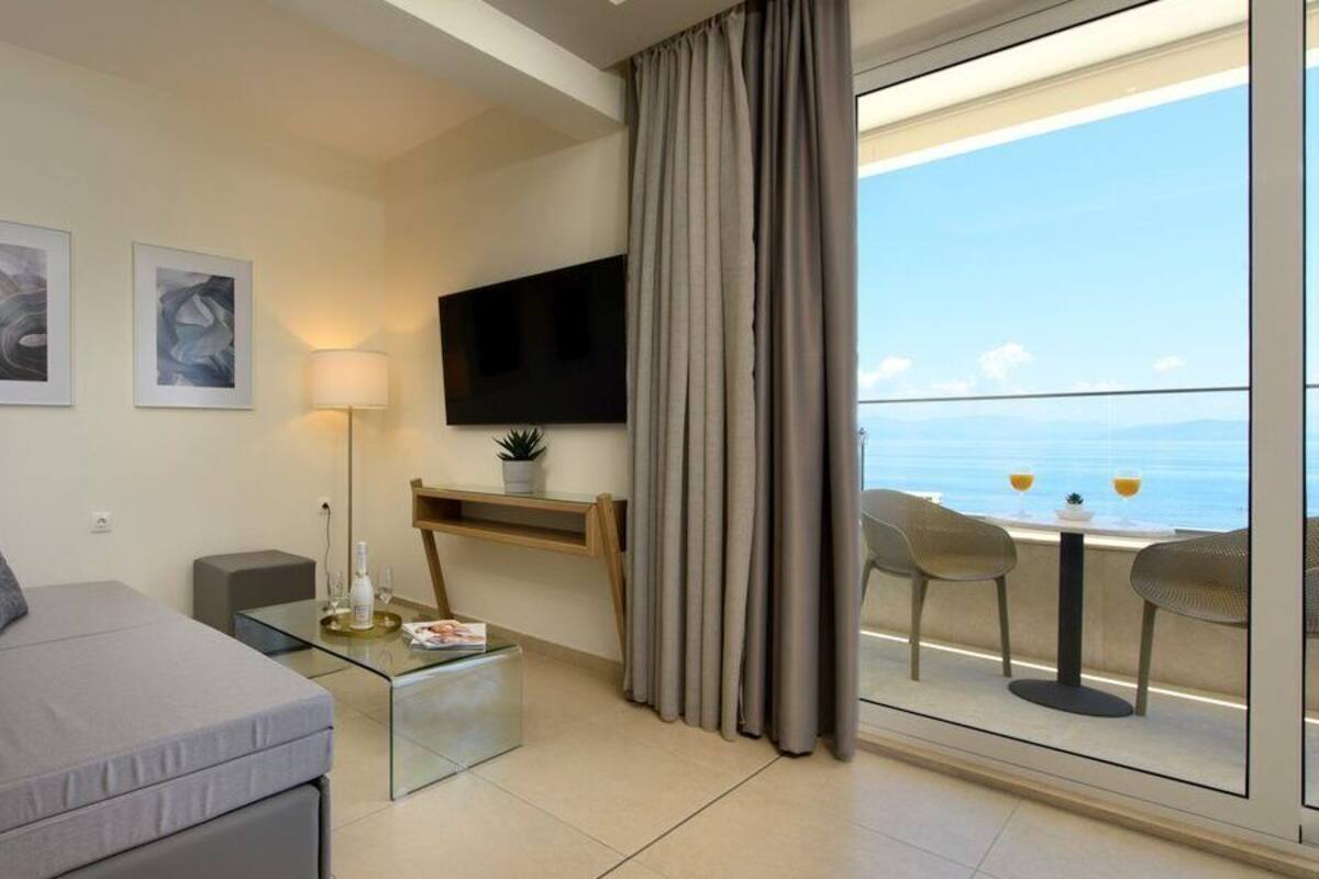 A modern living room with a sofa, a coffee table, a TV, and a balcony with a view of the sea.