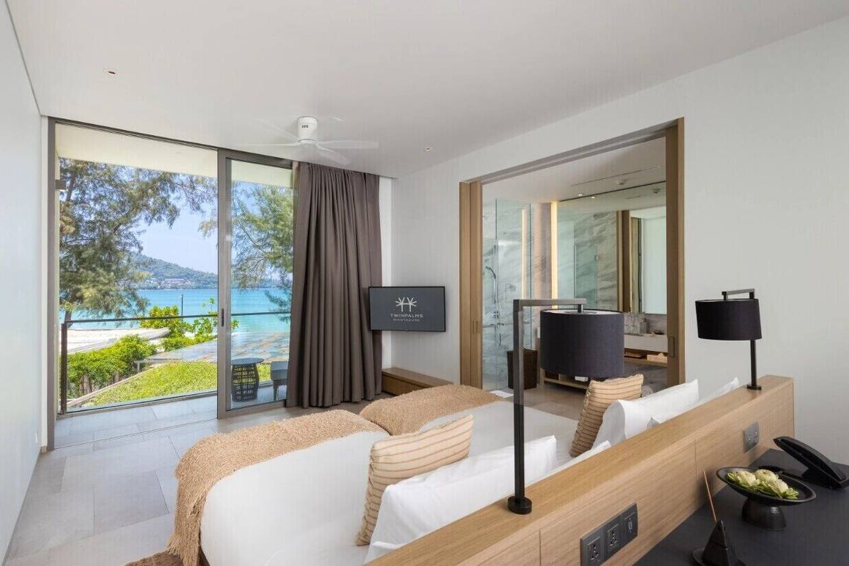 A modern hotel room with a large bed, a TV, a desk with a phone, and a view of the sea.