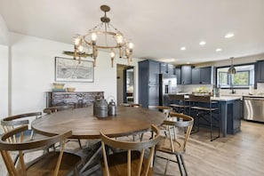 Une cuisine moderne avec une table ronde en bois, des meubles de couleur sombre et un lustre.