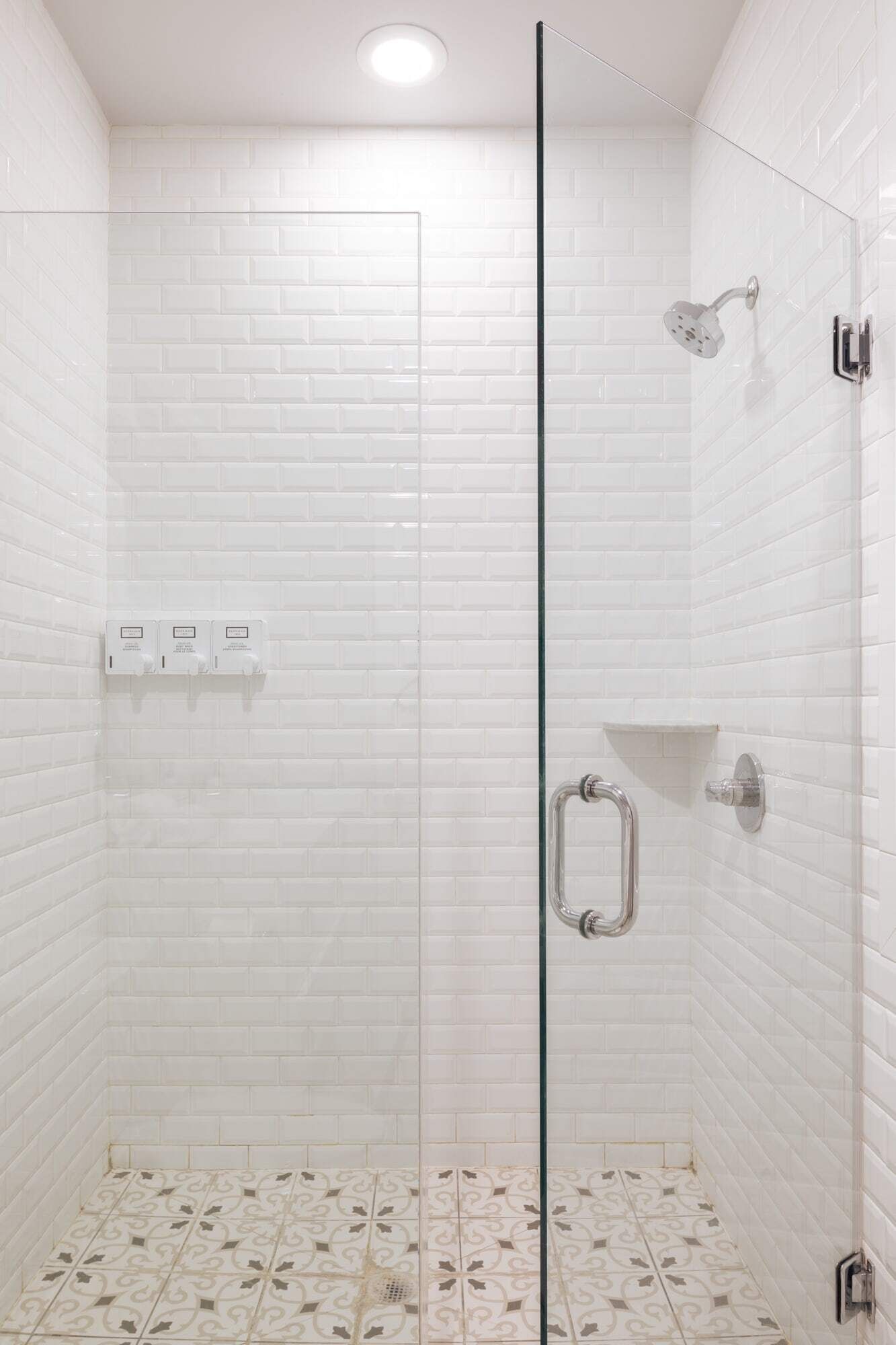 A shower with a glass door, white tiled walls, and a patterned floor.