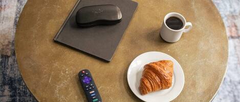 A round table with a remote control, a coffee cup, and a croissant on a textured surface.