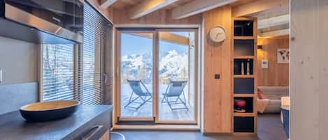 A modern kitchen with a large window, wooden ceiling, and a view of mountains.