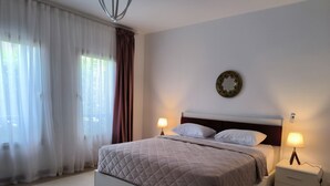 Un dormitori modern amb un llit gran, dues taules de nit amb làmpades, una placa decorativa mural i cortines translúcides.