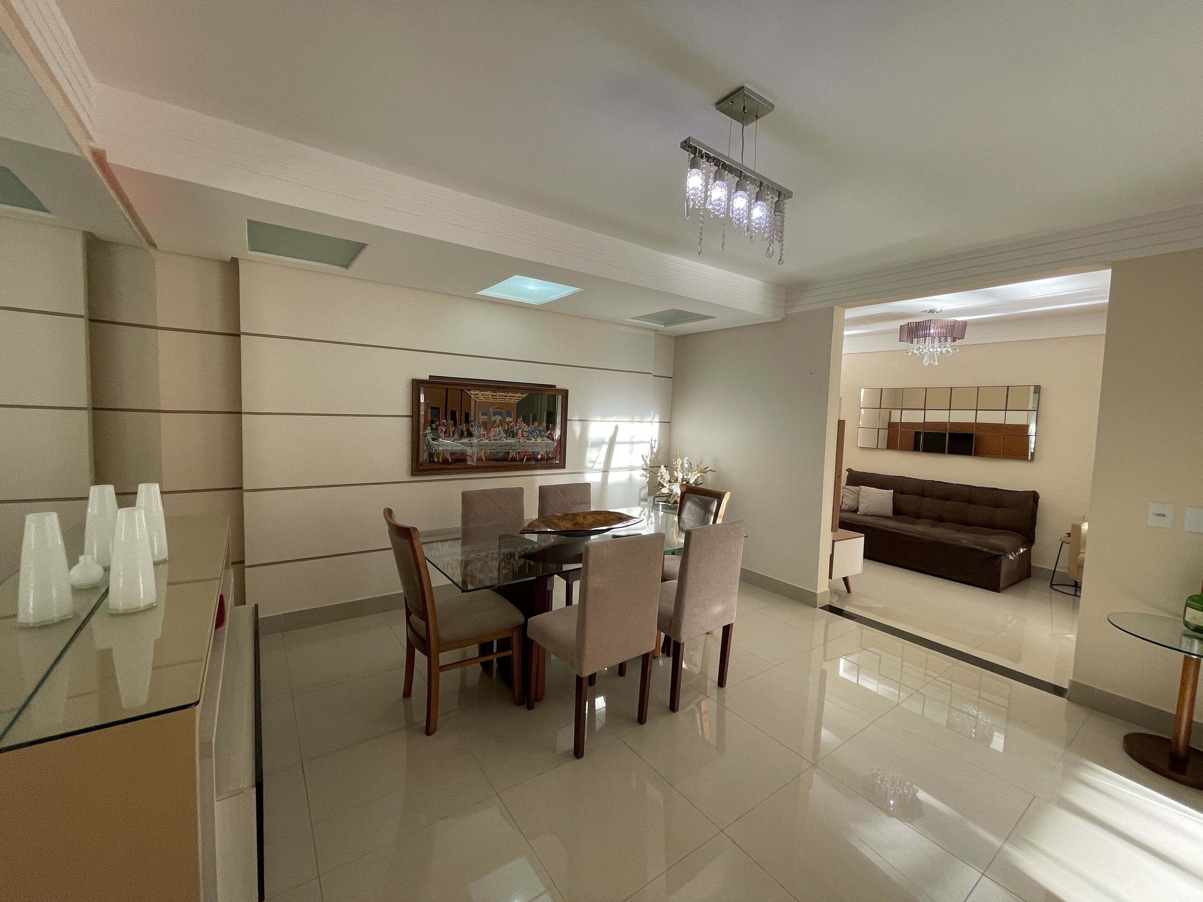 A modern dining area with a glass table, wooden chairs, and a chandelier.