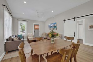 A spacious room with a wooden dining table, chairs, a sofa, and a large window with blinds. - The Grove Estate 8BD/7BA!  Perfect For Groups! (Fredericksburg)