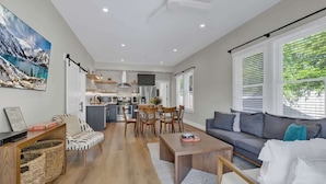 A spacious living area with a sofa, coffee table, and dining table. A kitchen with modern appliances is visible in the background. - The Grove Estate 8BD/7BA!  Perfect For Groups! (Fredericksburg)