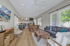 A spacious living area with a sofa, coffee table, and dining table. A kitchen with modern appliances is visible in the background. - The Grove Estate 8BD/7BA!  Perfect For Groups! (Fredericksburg)