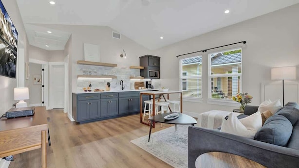 A modern kitchen with grey cabinets, a central island, and a dining area with a table and chairs. - The Grove Estate 8BD/7BA!  Perfect For Groups! (Fredericksburg)