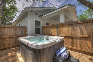 Een hottub in een achtertuin met een houten omheining, een overdekte patio en een huis op de achtergrond.