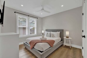 Een moderne slaapkamer met een bed, nachtkastjes, een plafondventilator en een raam met jaloezieën.