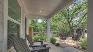 A covered patio with Adirondack chairs, a barbecue grill, and a fenced backyard. - The Grove Estate 8BD/7BA!  Perfect For Groups! (Fredericksburg)