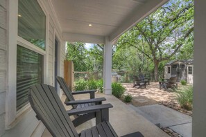 A covered patio with Adirondack chairs, a barbecue grill, and a fenced backyard. - The Grove Estate 8BD/7BA!  Perfect For Groups! (Fredericksburg)