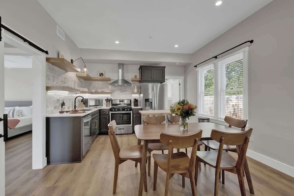 A modern kitchen with a dining area, built-in appliances, and large windows.