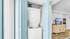 Une buanderie équipée d’une machine à laver et d’un sèche-linge superposés, d’un meuble en bois avec des tiroirs et d’un téléviseur posé sur un meuble en bois.