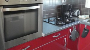 Une cuisine avec des meubles de rangement rouges, un four en acier inoxydable, une cuisinière à gaz et une machine à café.