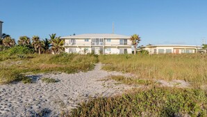 A beachfront property with a two-story building, a sandy path leading to the entrance, and palm trees in the background. - 2nd floor beach condo (Cocoa Beach)