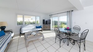 A modern living room with a sofa, a coffee table, a TV, and a dining area with chairs and a table. - Direct Oceanfront Beach Villa - Unit #1 (Cocoa Beach)