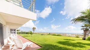 Un balcon avec des chaises blanches, une pelouse verdoyante et une vue sur la plage.