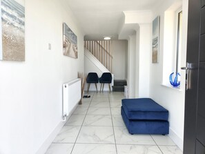 A hallway with a staircase, a radiator, two blue chairs, and a blue ottoman.