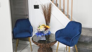 Uma escadaria com corrimãos de madeira, uma mesa de vidro com um arranjo floral e duas cadeiras azuis.