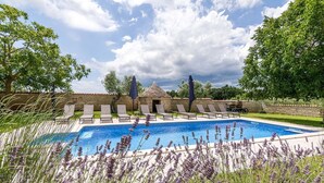 Ein Swimmingpool mit Liegestühlen und einem dahinterliegenden Steinhaus.
