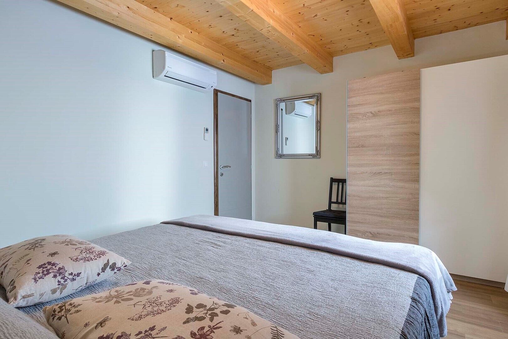 Une chambre à coucher comprenant un lit, un plafond en bois, un appareil de climatisation, une porte, un miroir et une chaise.