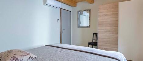 Une chambre à coucher comprenant un lit, un plafond en bois, un appareil de climatisation, une porte, un miroir et une chaise.
