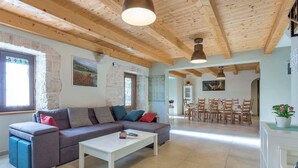 Ein geräumiges Wohnzimmer mit Holzboden, einem grauen Sofa mit Kissen, einem weißen Couchtisch und einem Essbereich mit Holzsesseln und einem Tisch.