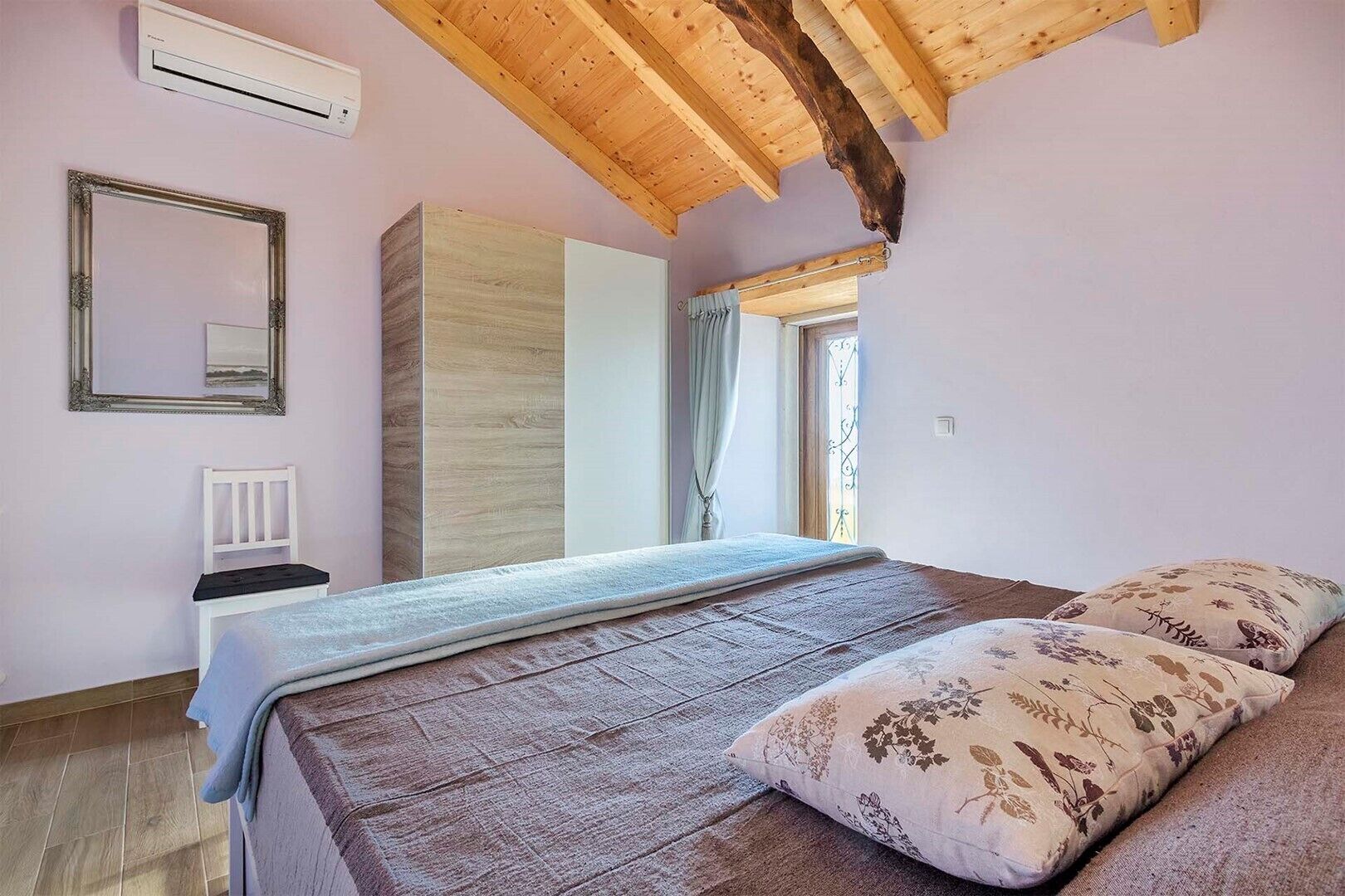 A bedroom with a bed, a chair, a wardrobe, and a mirror.