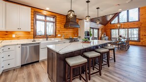 A spacious kitchen with a large island, wooden walls, and pendant lighting. - Mountain-Top Escape w/ Hot Tub, Views & Theater (McHenry)