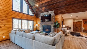 A cozy living room with a stone fireplace, large windows, and a wooden ceiling. - Mountain-Top Escape w/ Hot Tub, Views & Theater (McHenry)