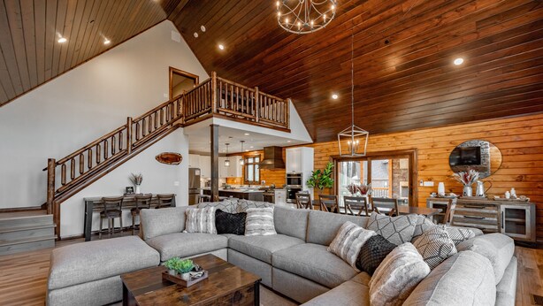 A spacious living area with a large sectional sofa, a wooden staircase, and a kitchen in the background. - Mountain-Top Escape w/ Hot Tub, Views & Theater (McHenry)