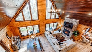 A spacious loft-style room with a large dining table, a sofa, and a fireplace. - Mountain-Top Escape w/ Hot Tub, Views & Theater (McHenry)