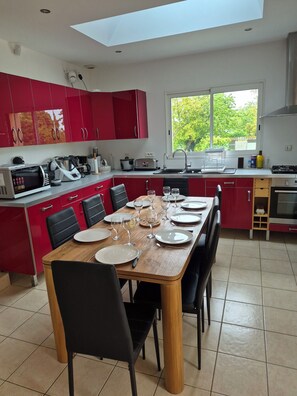 A modern kitchen with red cabinets, a dining table set for six, and a large window providing a view of greenery outside.