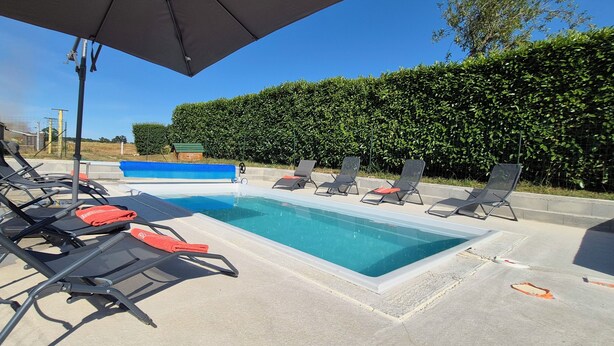 Ein Poolbereich mit Liegestühlen, einer blauen Schwimmanlage und einer Hecke im Hintergrund.