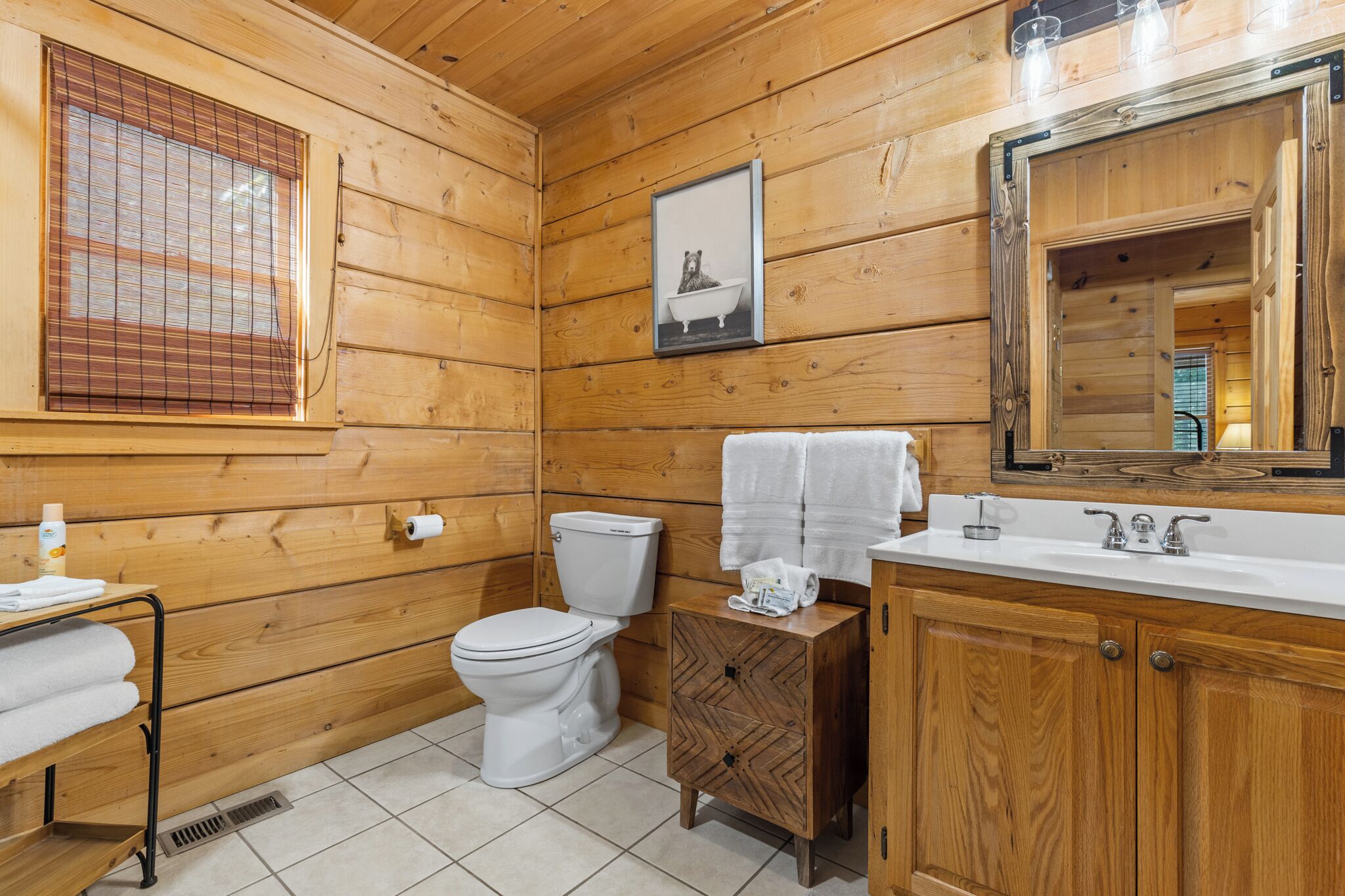 A wooden cabin bathroom with a toilet, sink, and mirror.