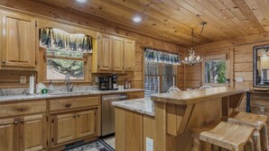 A wooden cabin kitchen with wooden cabinets, a central island, and a chandelier. - Bear Shenanigans in Blue Ridge (Blue Ridge)