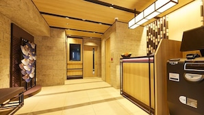 A hotel lobby with a reception desk, a vending machine, and a wall-mounted light fixture. - MONday Apart Premium Hamamatsucho (Tokyo)