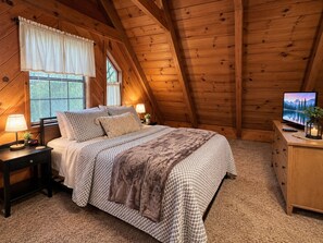 A cozy bedroom with a bed, nightstands, a TV, and a window with curtains.