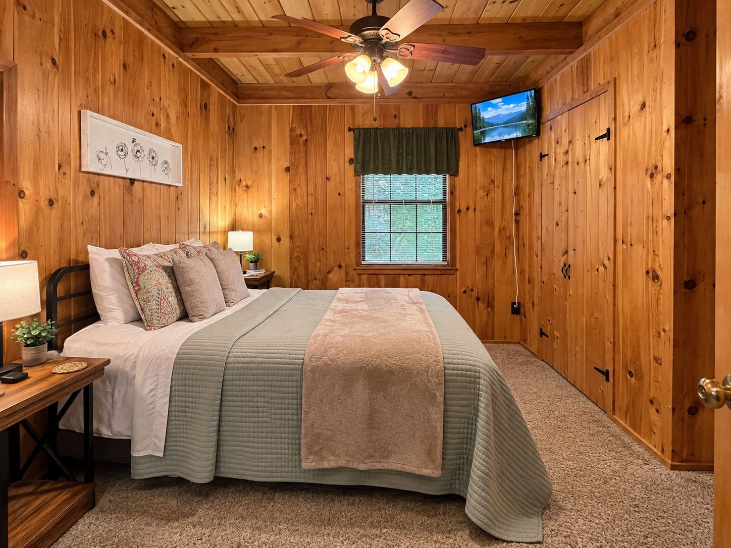 A bedroom with a bed, a nightstand, a lamp, a television, and a window with blinds.