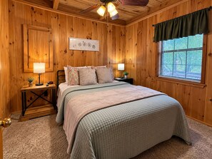Une chambre à coucher aux murs lambrissés, avec un lit, des lampes de chevet, une horloge et une fenêtre équipée de stores.