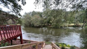A wooden staircase leading down to a river, surrounded by trees and a wooden deck with chairs. - Bigfoot's River Retreat (Mineral Bluff)