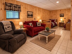 Um quarto aconchegante com um sofá vermelho, uma poltrona escura, piso de madeira e uma cama com um cobertor xadrez vermelho e preto.