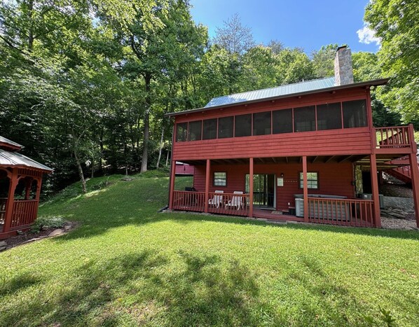 A two-story red cabin with a covered porch, a stone chimney, and a small deck. - Bigfoot's River Retreat (Mineral Bluff)